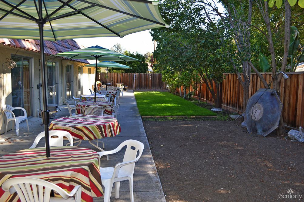 A backyard patio with tables, umbrellas, and chairs next to a garden and a wooden fence.