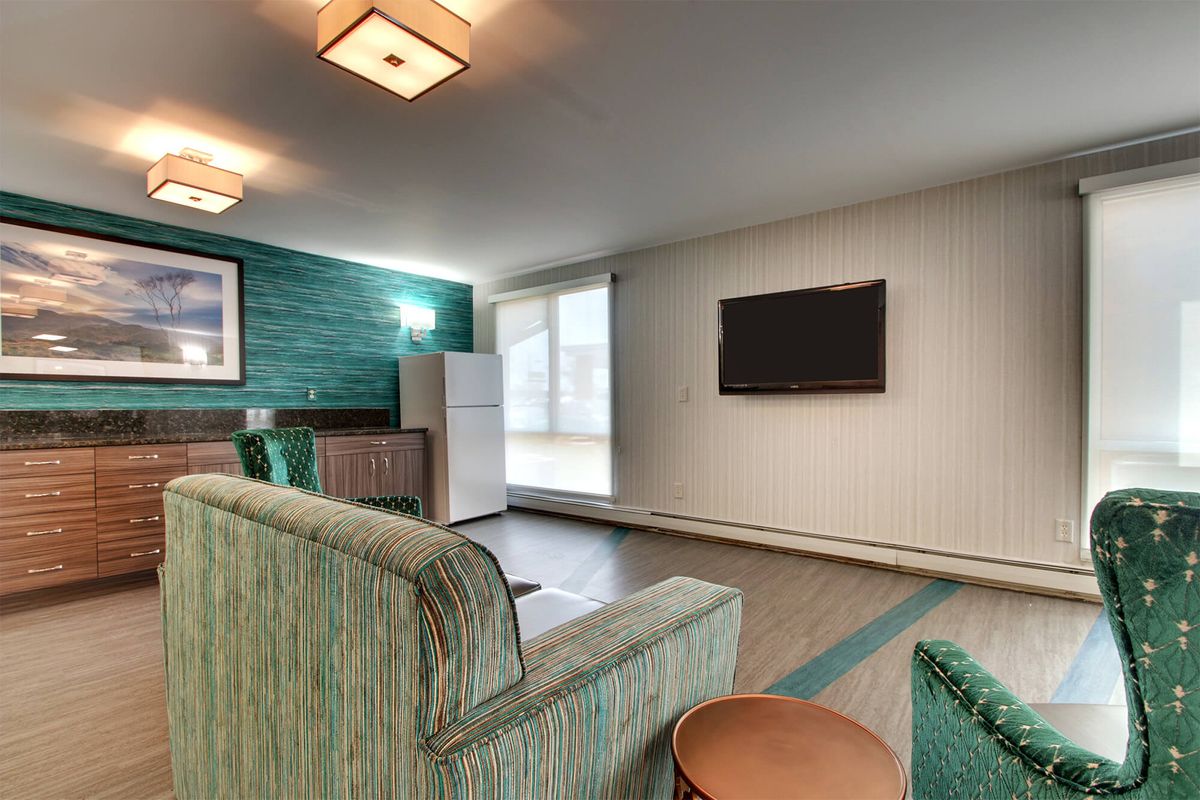 A modern apartment living room with a green color scheme, featuring a sofa, wall-mounted television, and a refrigerator.