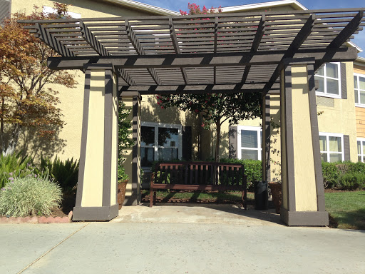 A welcoming entrance featuring a pergola and a bench, surrounded by greenery.