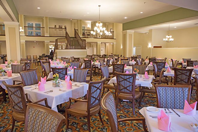 An elegantly decorated dining room with neatly arranged tables and chairs, featuring pink napkins and a chandelier.