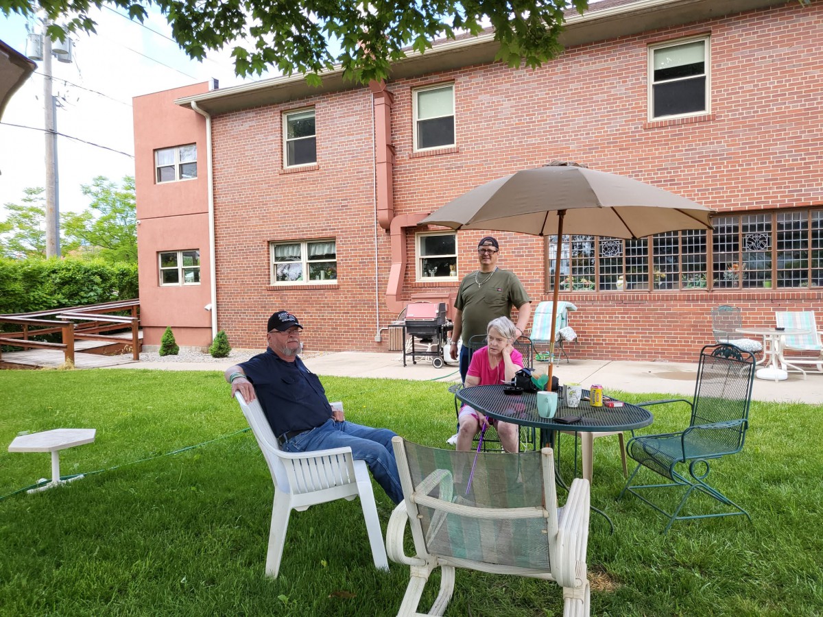 A group of people relaxing in a backyard with lawn chairs and a patio set in front of a brick house.