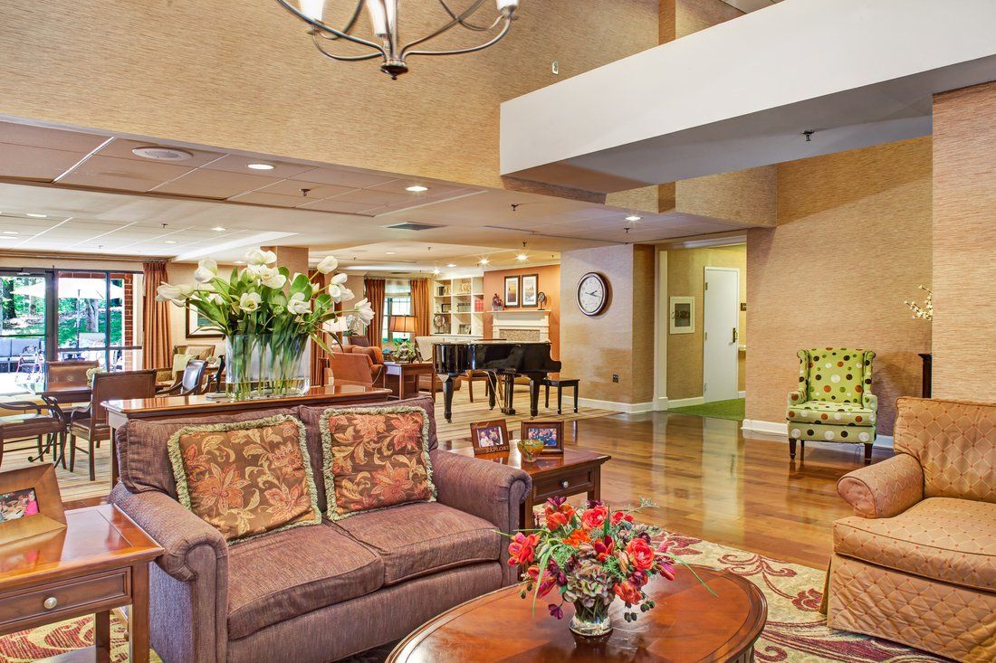 A spacious and elegantly decorated living room featuring a sofa, coffee table with flowers, grand piano, and wood flooring.