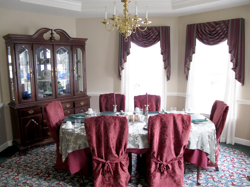 A formal dining room with a decorated table, elegant chandelier, and red chair covers.