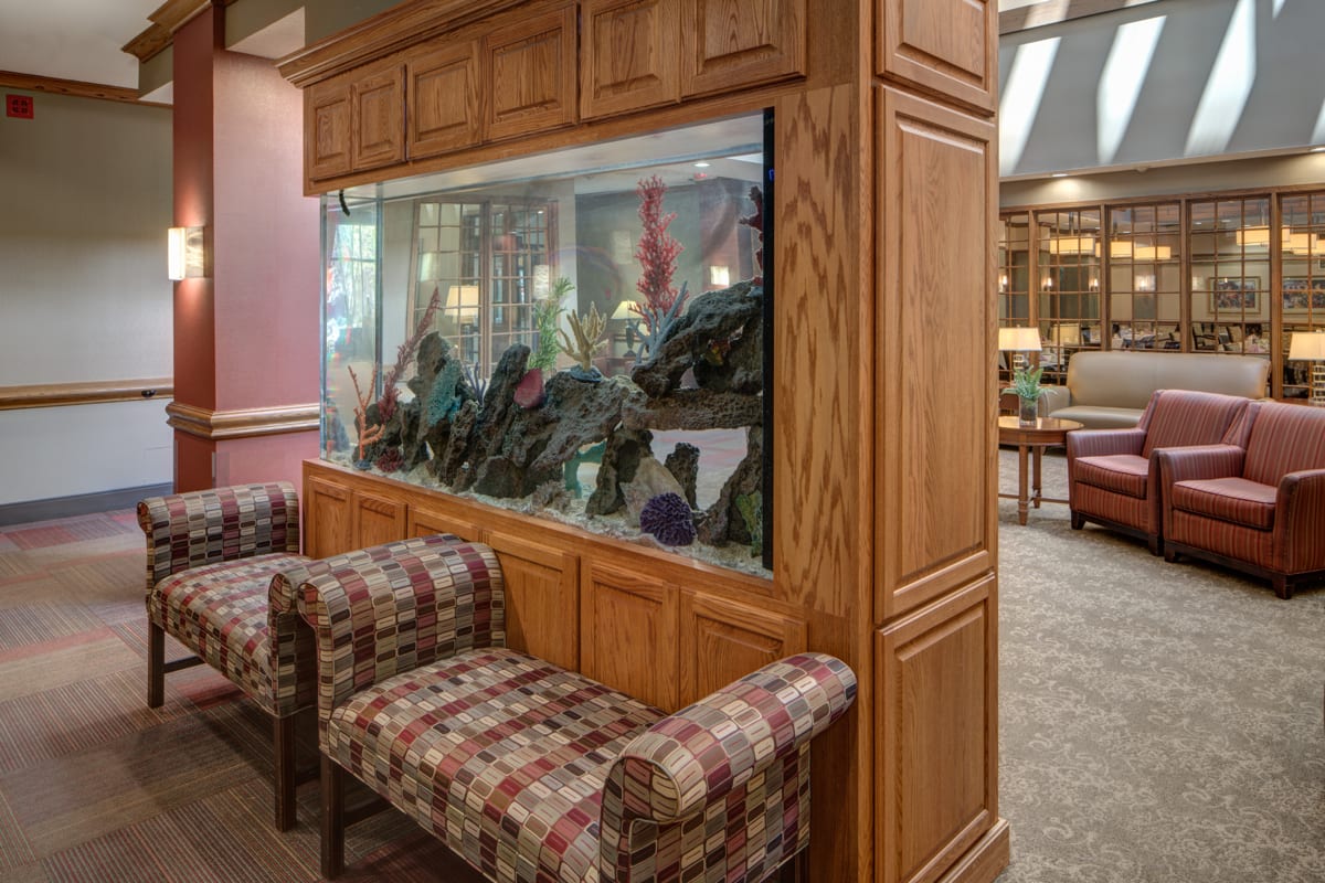 A cozy lobby features a large fish tank integrated into wooden cabinetry, flanked by patterned chairs.