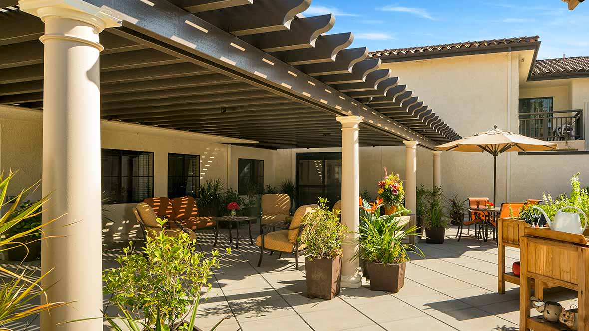 A sunny patio with a pergola, featuring comfortable outdoor seating and potted plants.