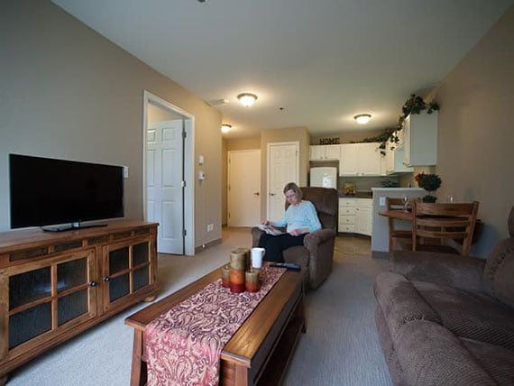 A cozy apartment living room with modern decor, featuring a person sitting on a sofa and watching television.