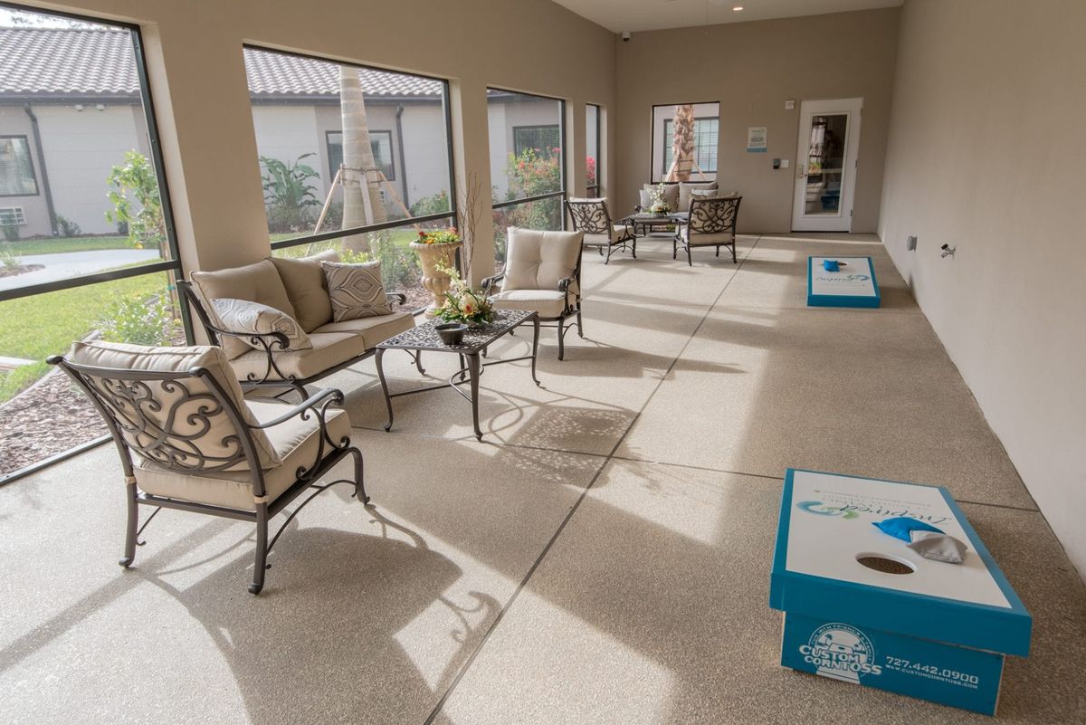 A bright sunroom featuring comfortable patio furniture and a cornhole game setup.