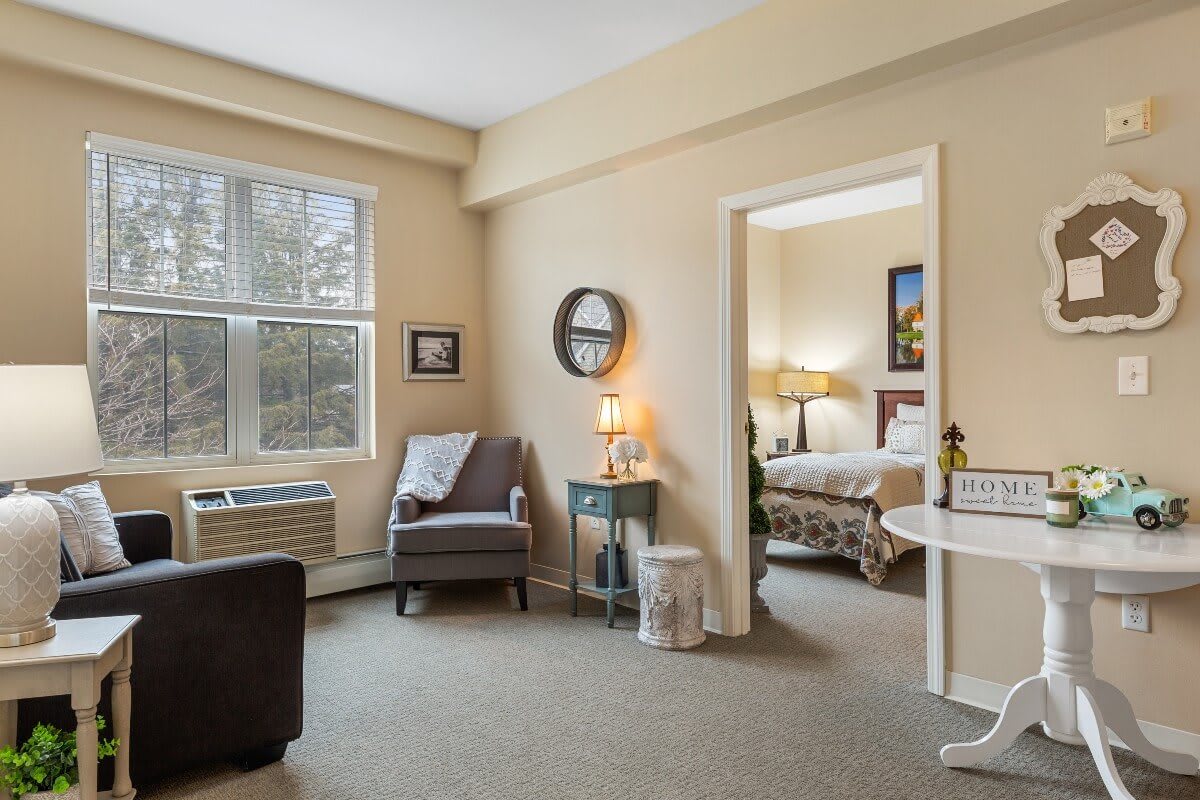 A cozy living room with a view into a bedroom, featuring comfortable furniture and warm lighting.