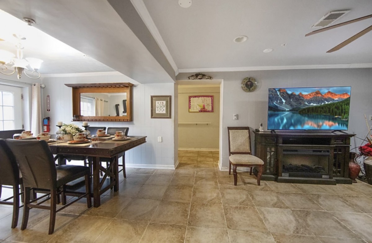 A cozy living room with a dining area, featuring a TV, wooden table, chairs, and various decorative elements.