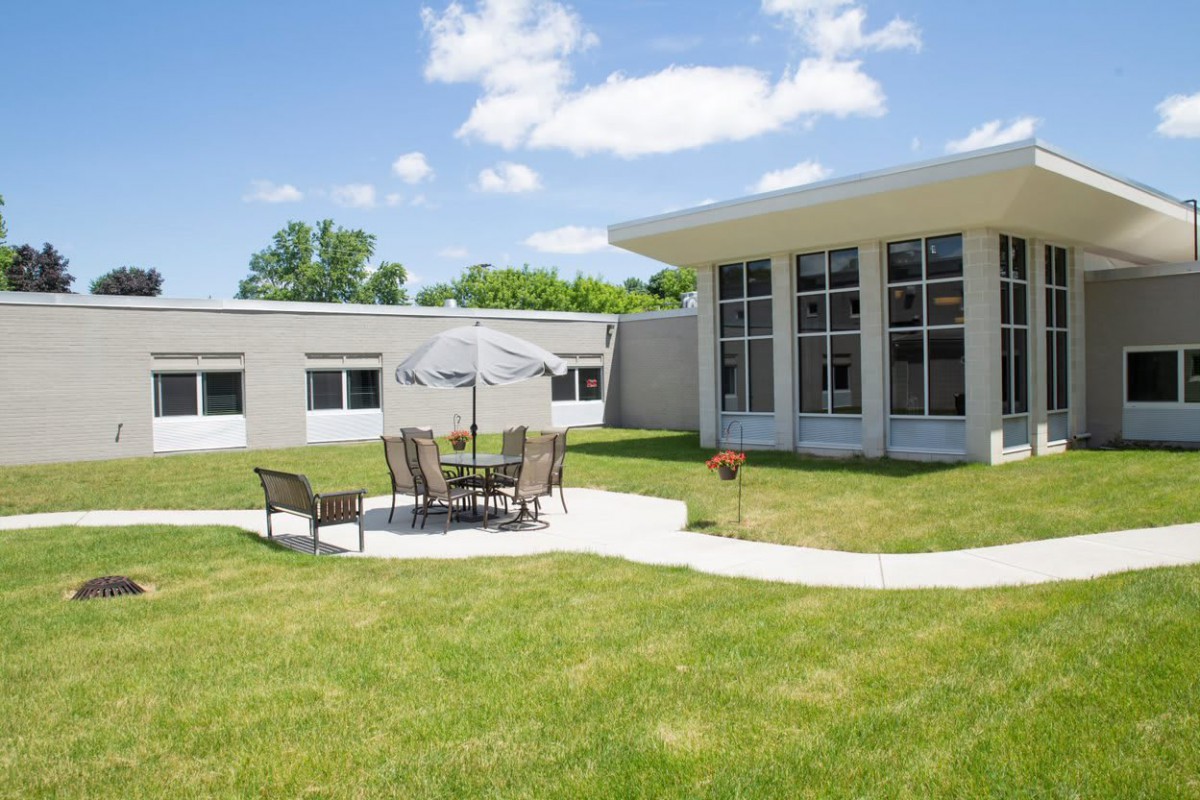 A courtyard with patio furniture and an umbrella beside a modern building under a clear blue sky.