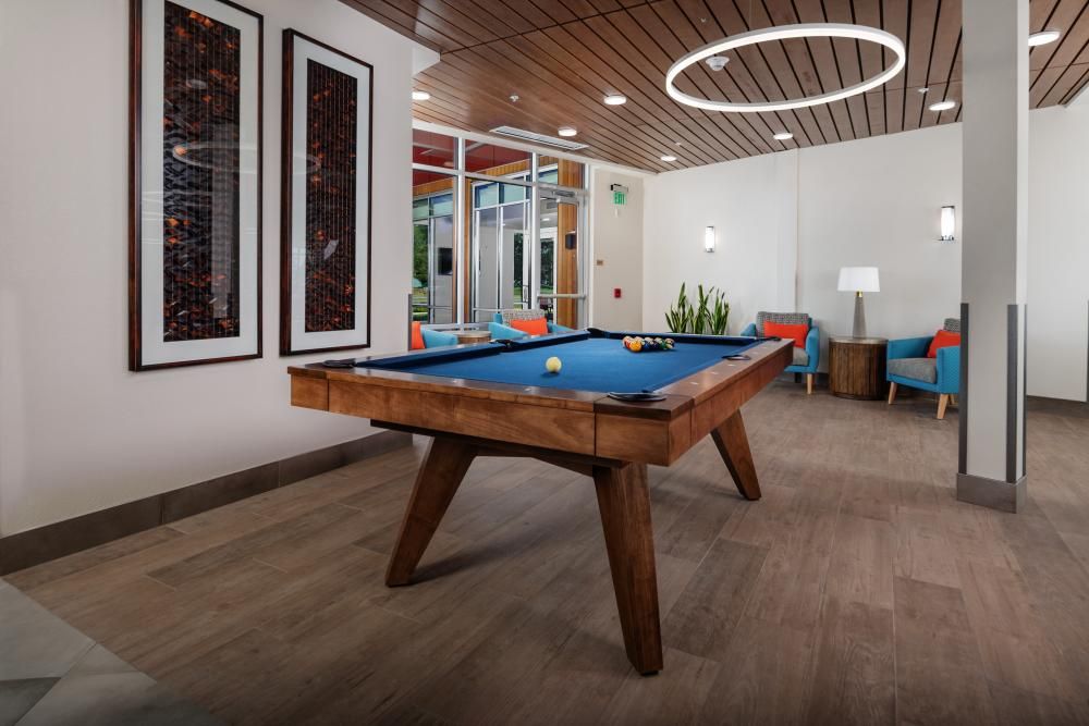 A modern game room featuring a stylish pool table with blue felt, surrounded by contemporary decor and comfortable seating.