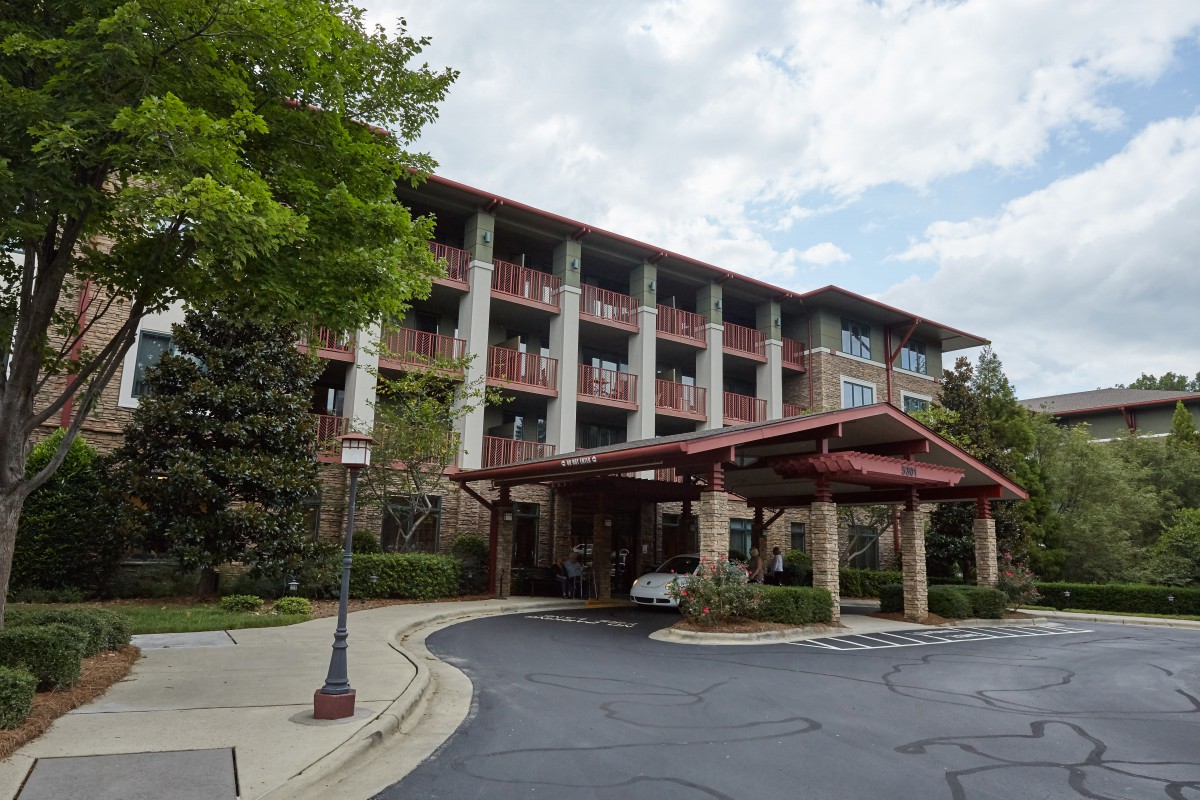 A hotel building with a grand entrance surrounded by trees under a cloudy sky.