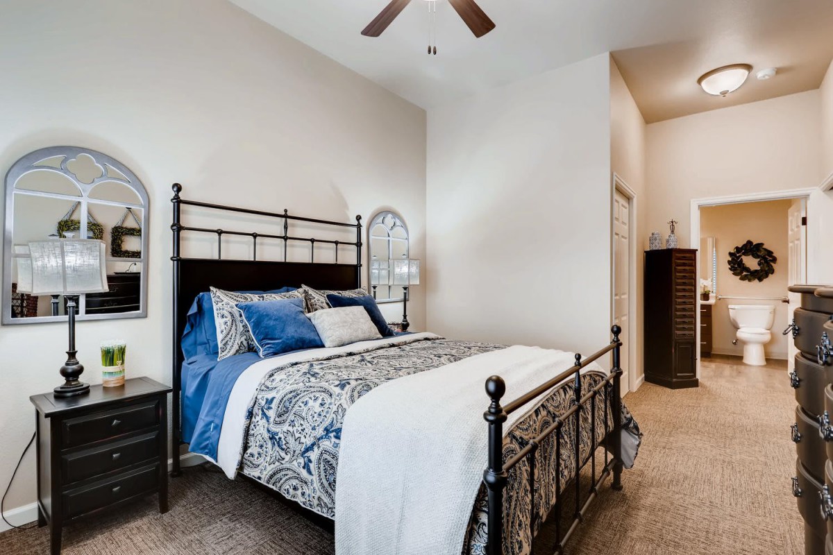A cozy bedroom featuring a metal bed frame with patterned bedding and a ceiling fan.