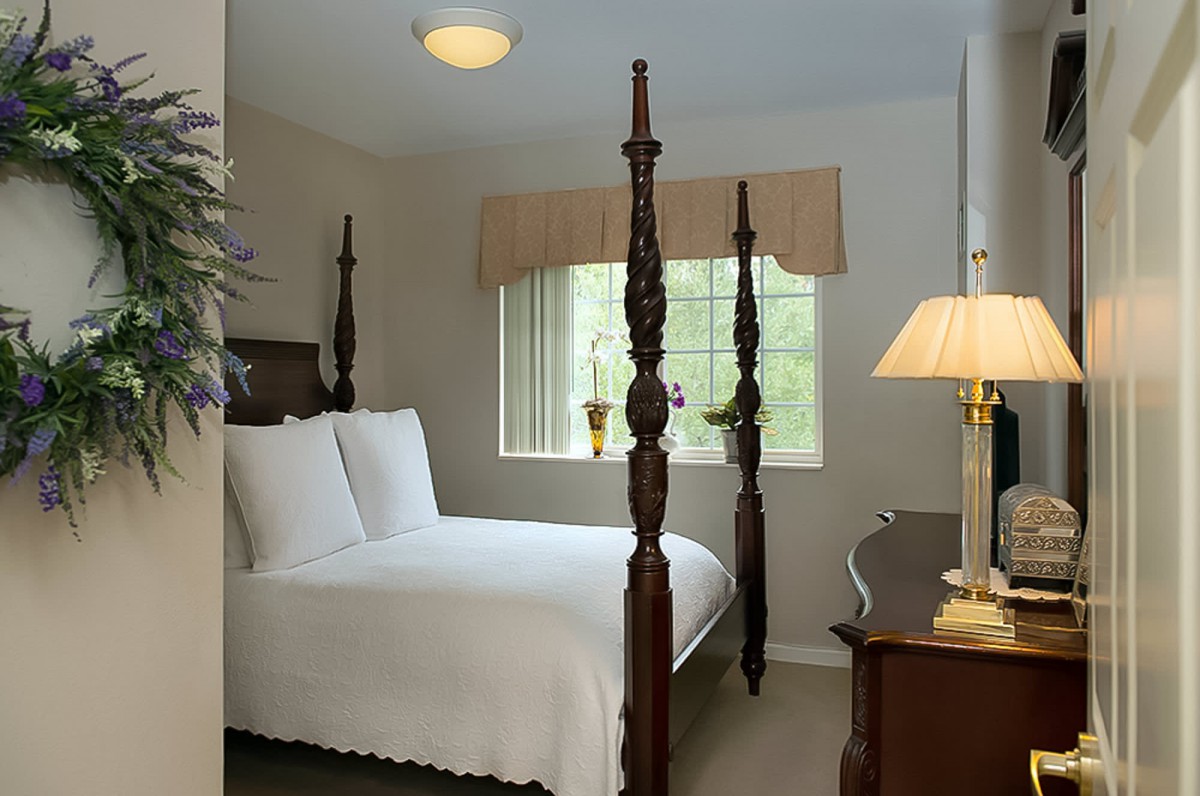 A cozy bedroom with a four-poster bed and a warm lamp by the window.