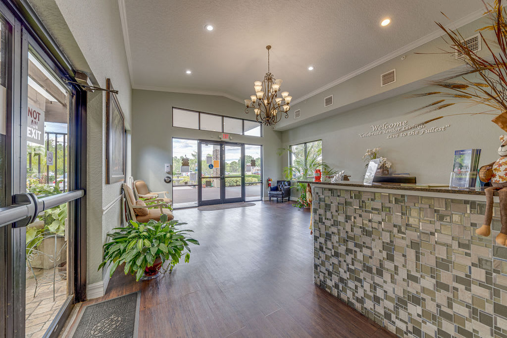 A modern reception area with a chandelier and plants, featuring elegant wood flooring and a welcoming atmosphere.