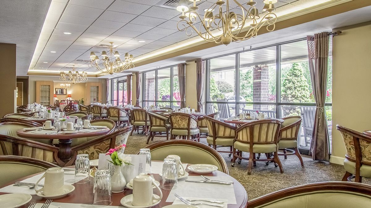An elegant dining room with well-set tables and large windows, featuring chandeliers.