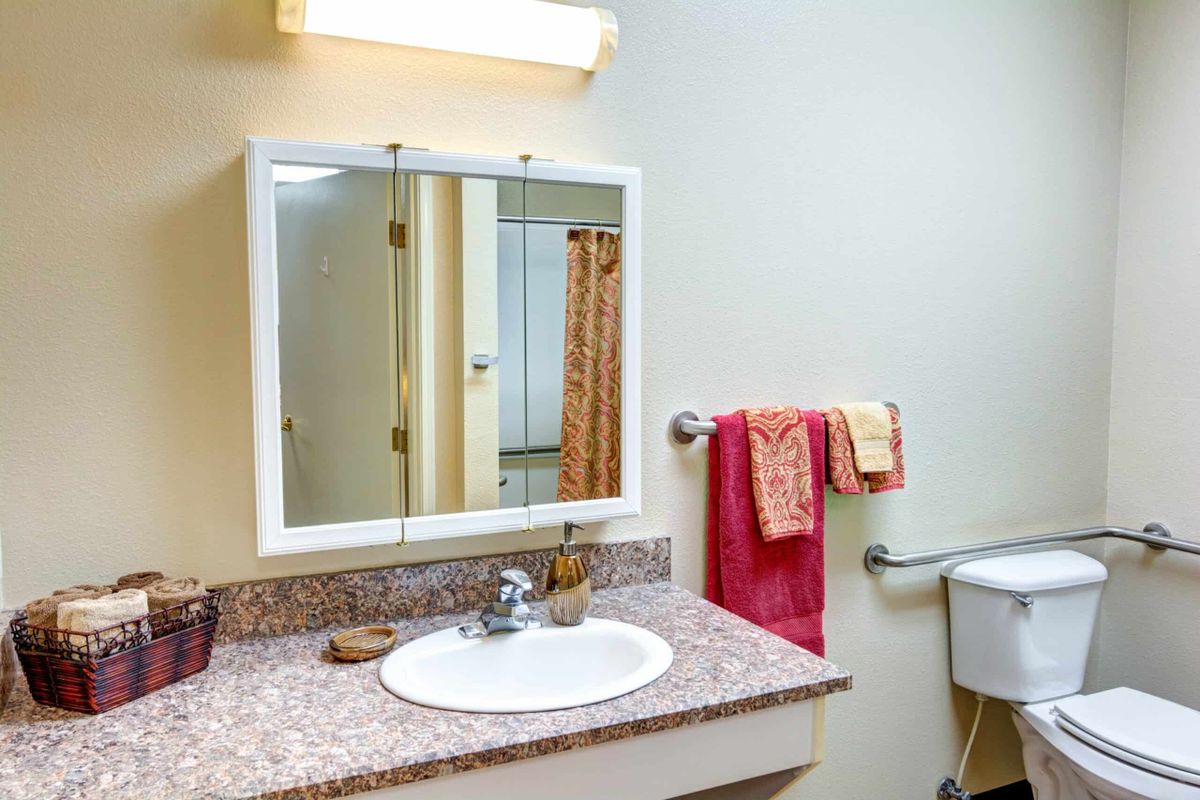A clean and organized bathroom featuring a sink with a mirror, towels on the rack, and a toilet.