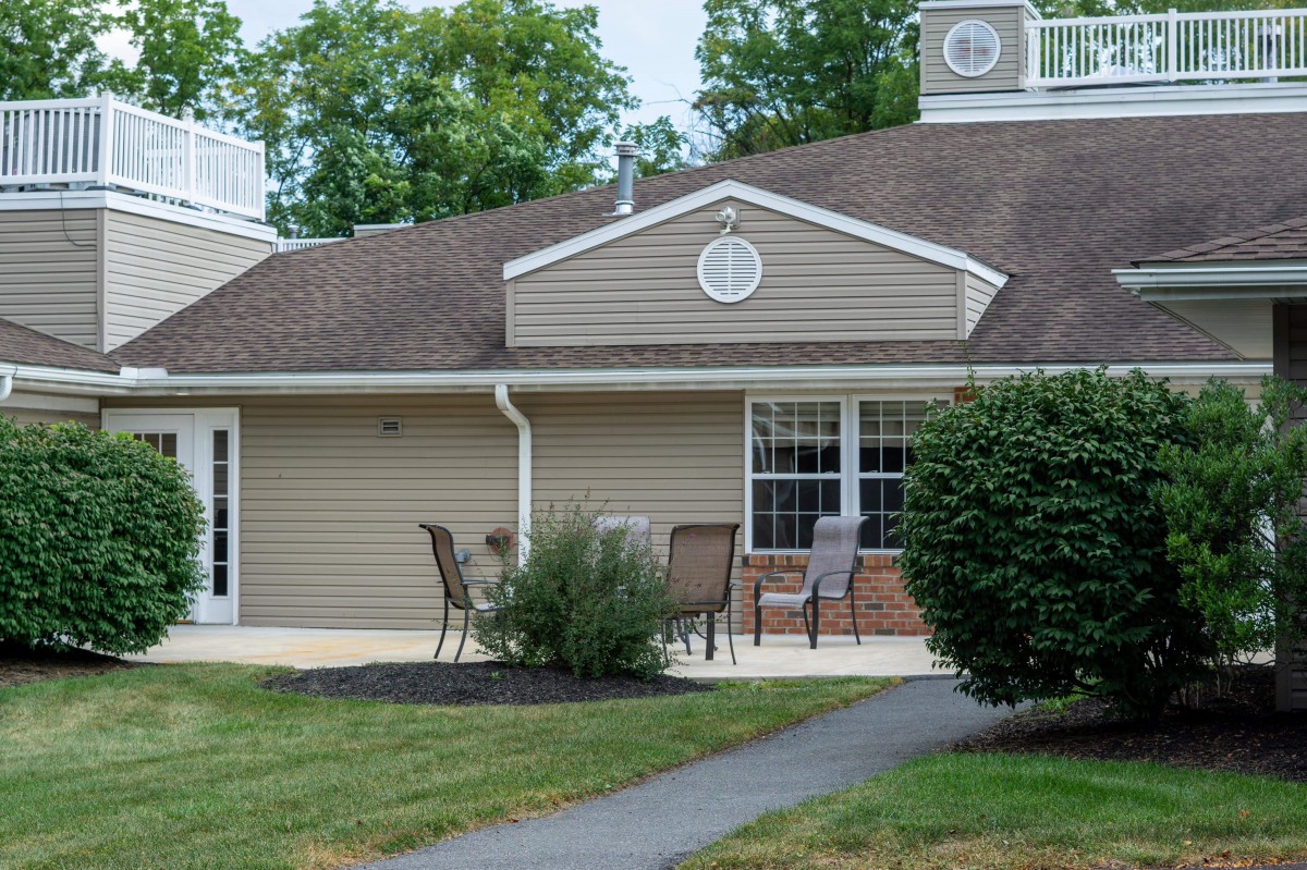 A residential house with a patio, outdoor chairs, and surrounding shrubs.