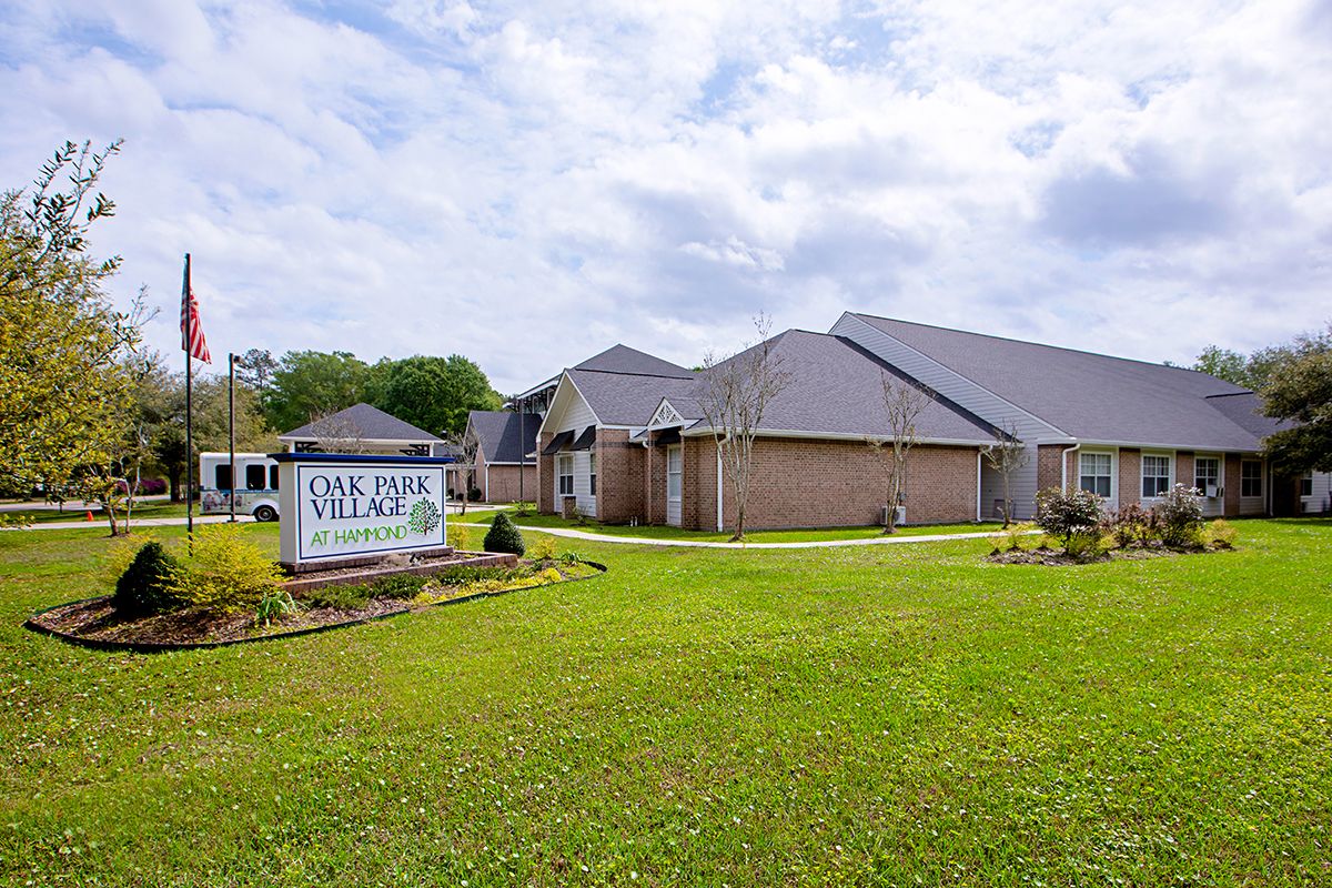A suburban building with a well-maintained lawn and a sign reading 'OAK PARK VILLAGE AT SLOID SPRINGS'.