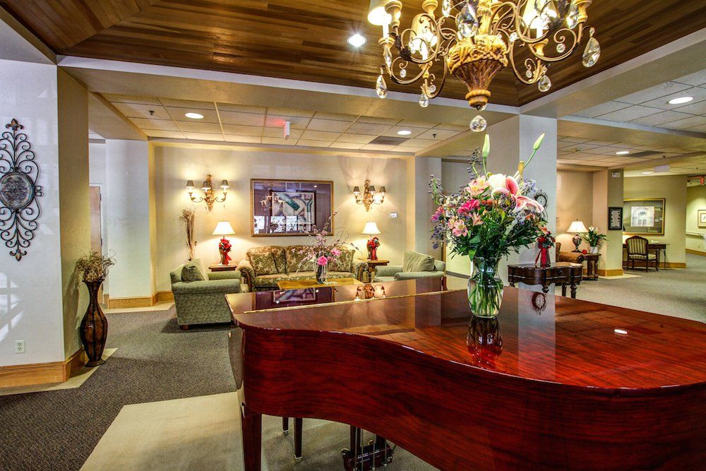 A luxurious hotel lobby featuring a grand piano, elegant chandelier, and comfortable seating area adorned with flowers.