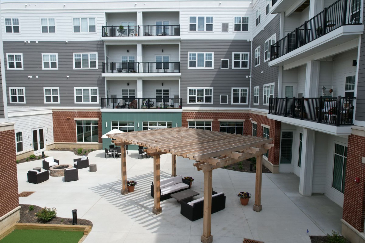 A modern apartment complex with a central patio area featuring outdoor seating and a pergola.