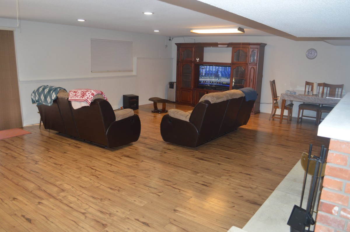 Spacious living room with hardwood flooring, featuring cozy sofas and a television setup, adjacent to a dining area.