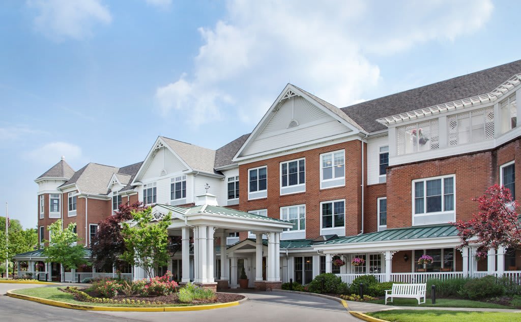 A picturesque view of a large residential building with traditional architecture, featuring a brick facade and white columns at the entrance under a clear blue sky.