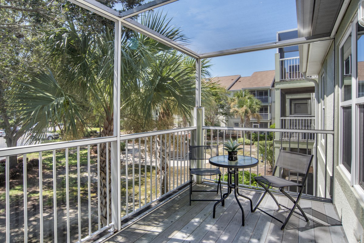 A cozy balcony with a small table and chairs overlooking palm trees and apartments.