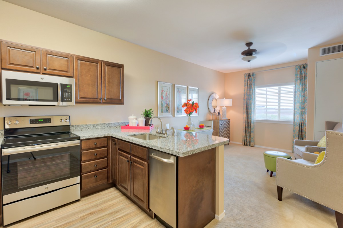 An open-plan kitchen and living room with modern interior design, featuring wood cabinets and stainless steel appliances.