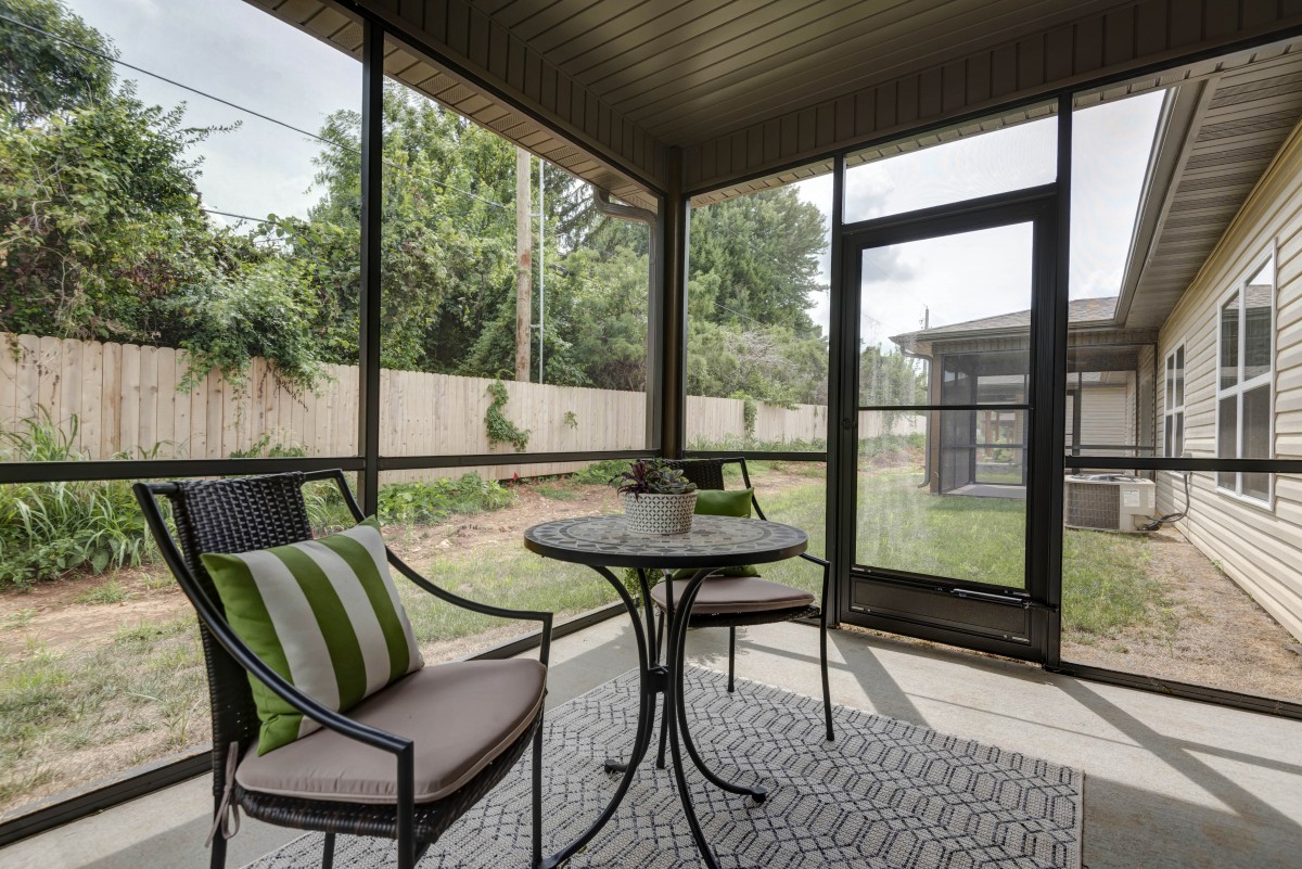 Cozy screened-in porch with a garden view, featuring a small table and chairs for relaxation.
