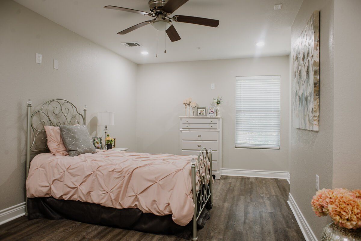 A minimalist bedroom with a metal bed frame, wooden dresser, and ceiling fan.