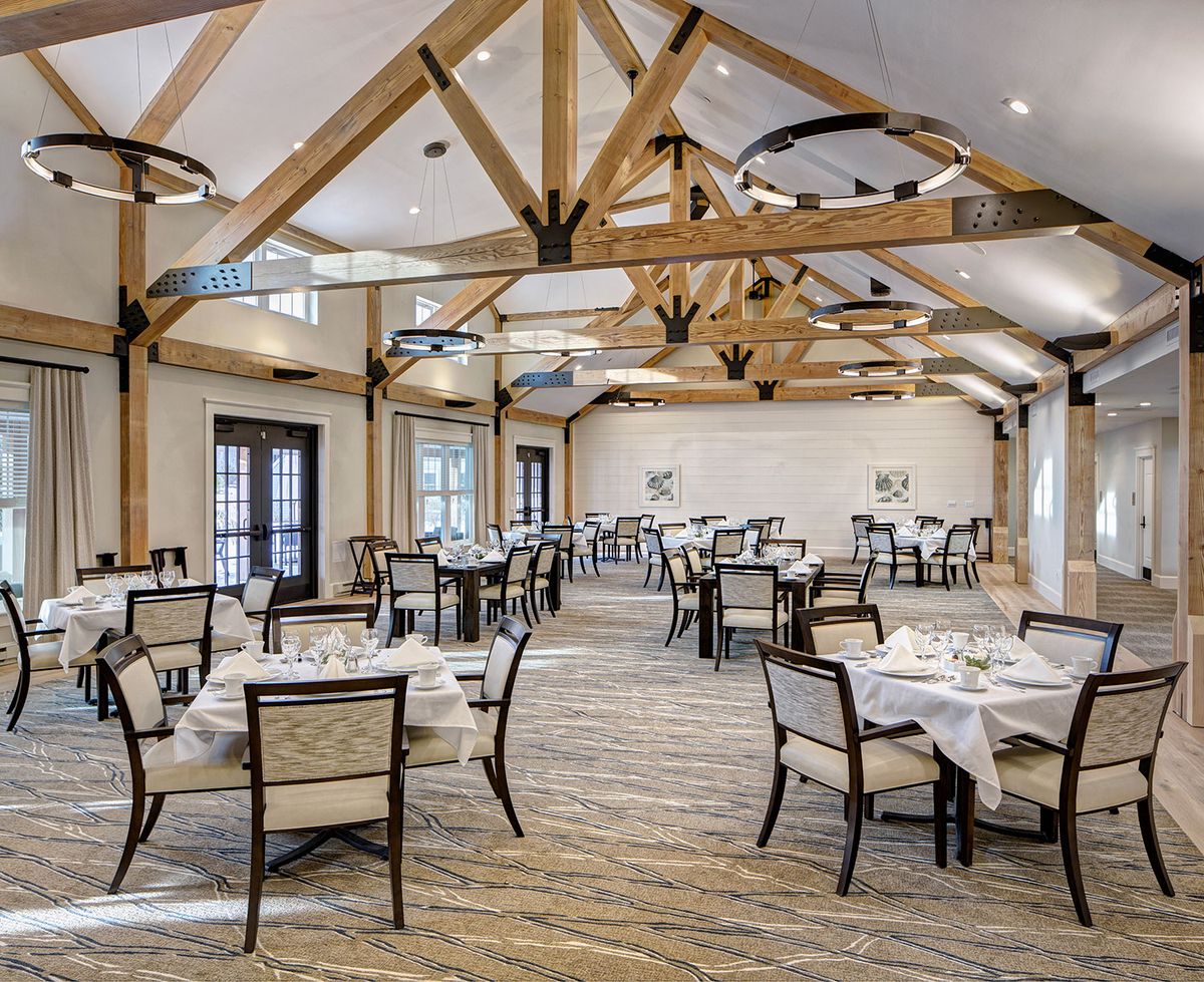 An elegant restaurant interior with neatly arranged tables and chairs, featuring exposed wooden beams.