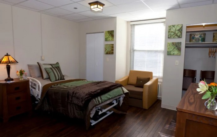 A cozy bedroom with a single bed, armchair, and window providing natural light.