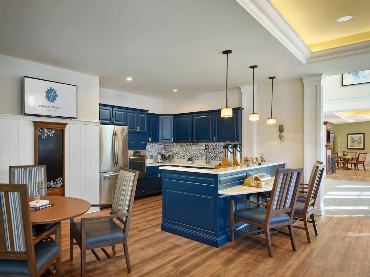 A modern kitchen with blue cabinets and an adjacent dining area, featuring wood flooring and pendant lighting.