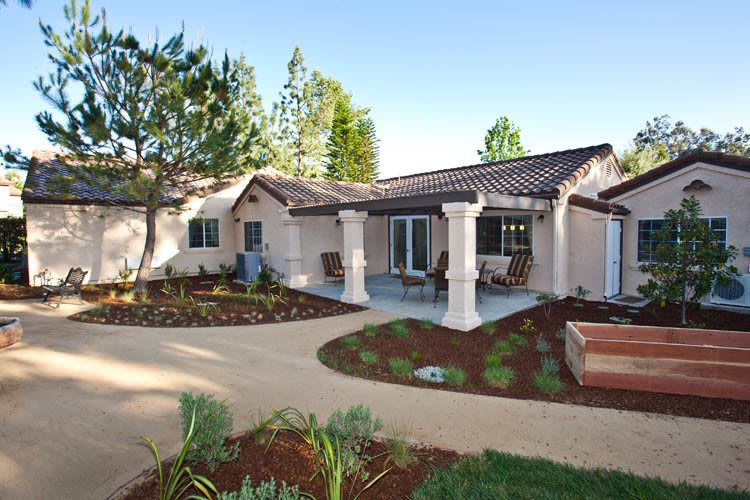 A beautifully landscaped front yard featuring a modern house with a patio and garden.