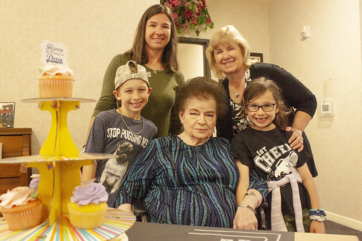A family group gathered together with a cake, smiling for a photo during a celebration.