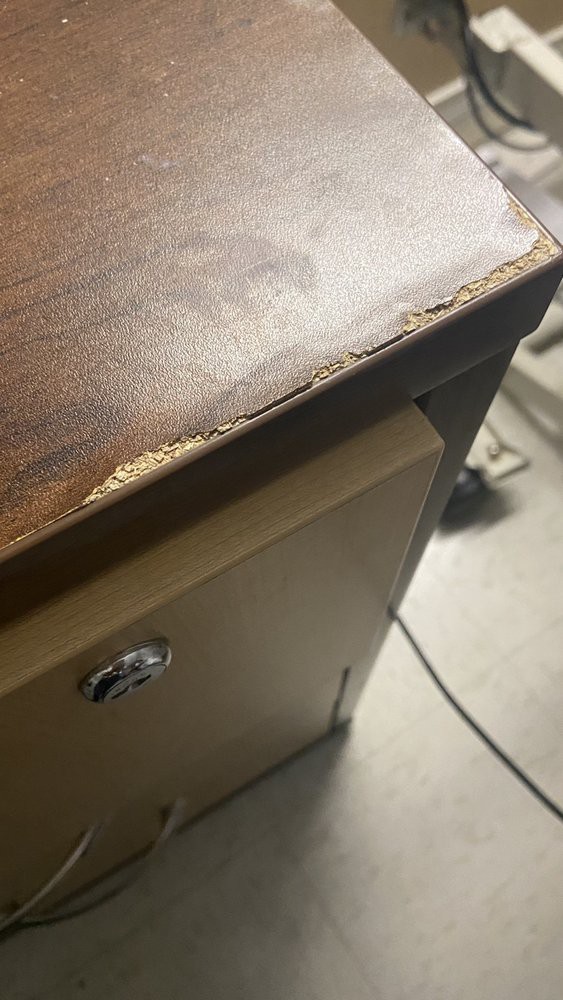 A close-up of a damaged wooden desk corner in an office setting.