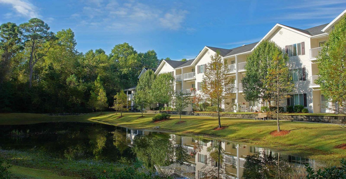 A serene apartment complex by a tranquil lake, surrounded by lush greenery.