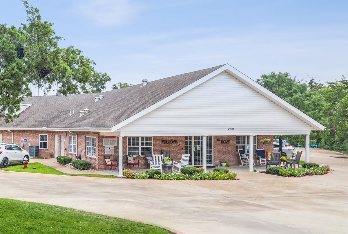A brick residential house with a covered porch and surrounding greenery.