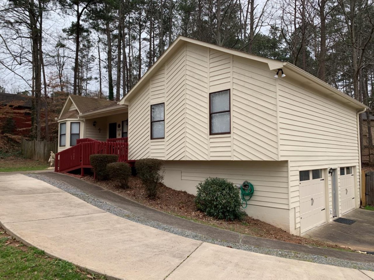 A single-story house with a red front porch, surrounded by trees and featuring a driveway.