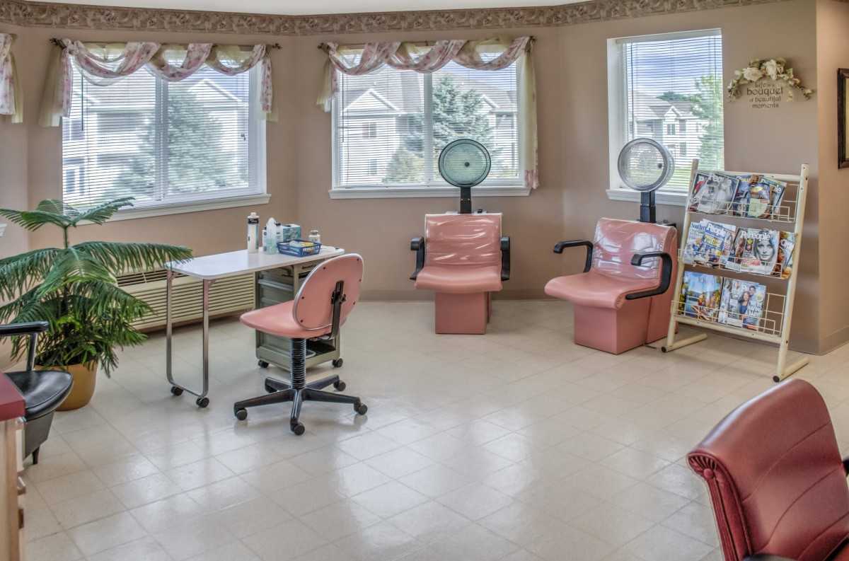 An empty salon room with pink chairs and hair dryers, featuring large windows.