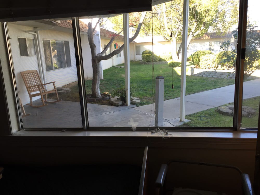 A view through a window overlooking a courtyard with grass and trees on a sunny day.