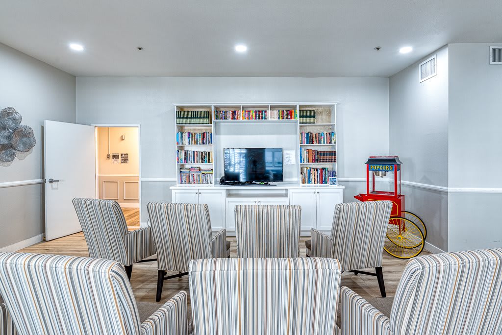 A cozy home theater setup with rows of chairs facing a television and bookshelves, featuring a popcorn machine.