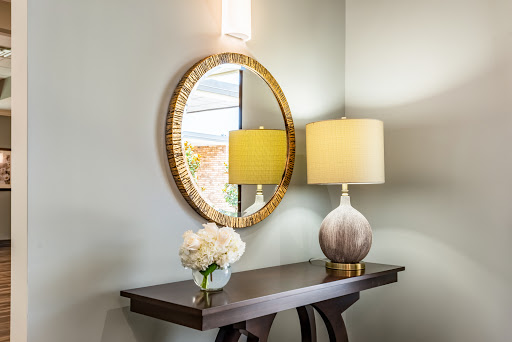 A beautifully styled entryway featuring a round mirror, a soft yellow lamp, and a floral arrangement on a console table.