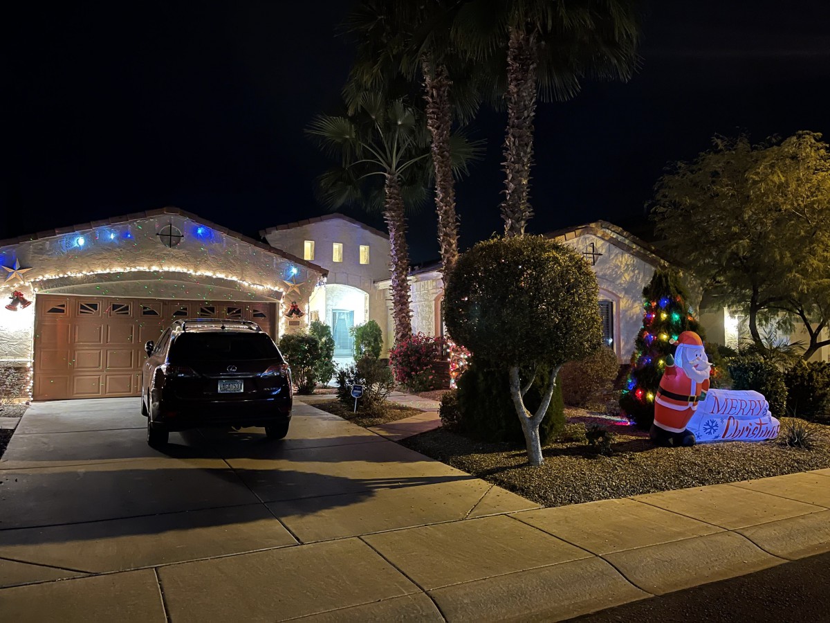 A house decorated with Christmas lights and an inflatable Santa beside a car during the night.