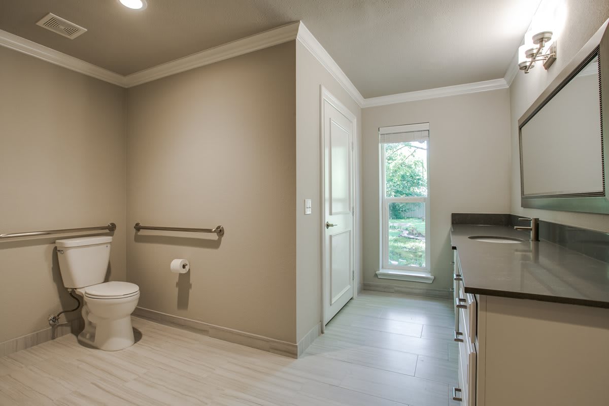 A modern, minimalist bathroom featuring a toilet with grab bars and a sink.