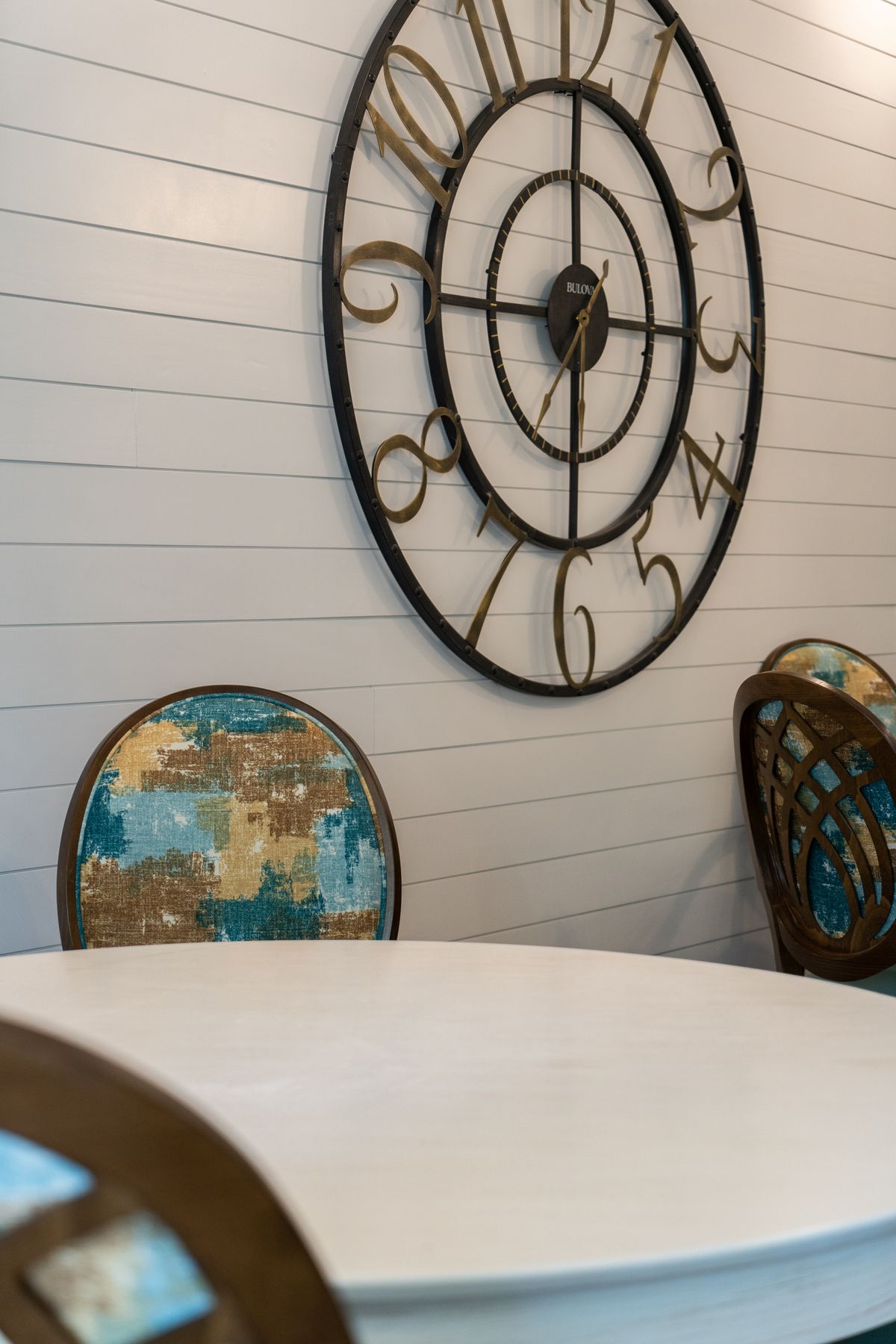 A cozy dining area featuring a large wall clock and patterned chairs.