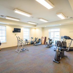 A well-lit gym with various exercise equipment including treadmills, ellipticals, and stationary bikes.