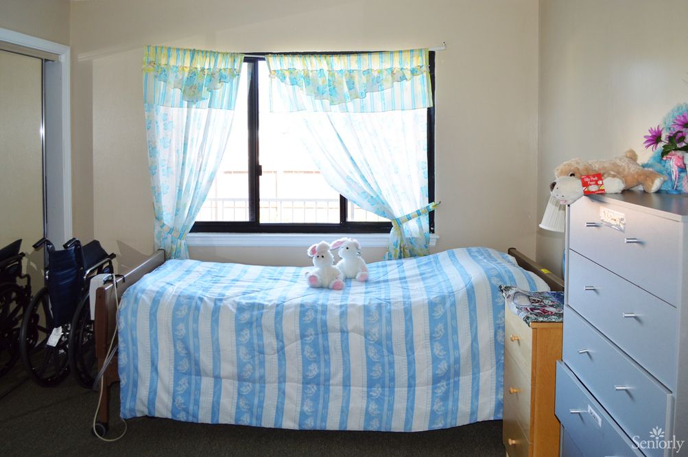 A neatly made bed with blue and white striped bedding, positioned next to a window with sheer curtains and a set of towels placed on top.