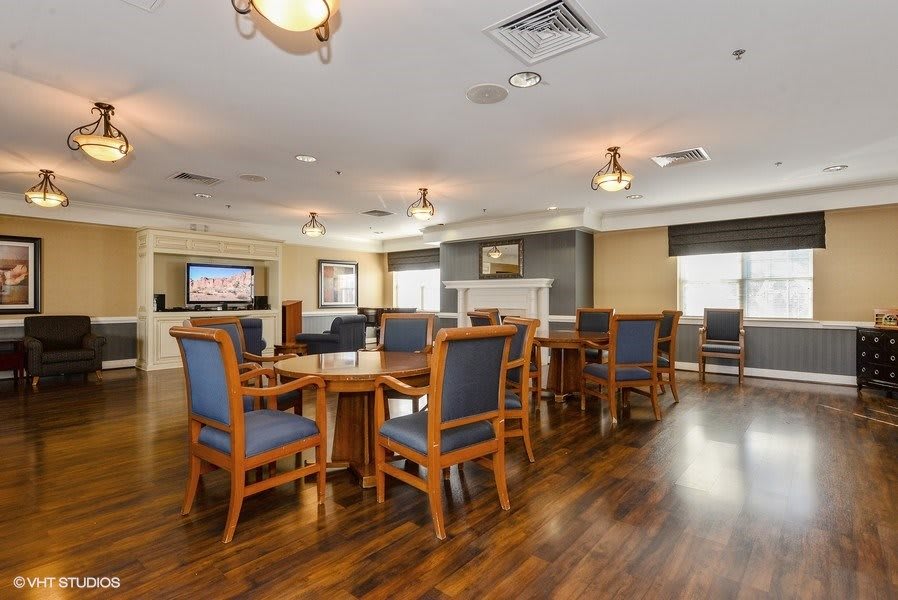 A spacious dining area with wooden tables and blue upholstered chairs, featuring a television and a fireplace.